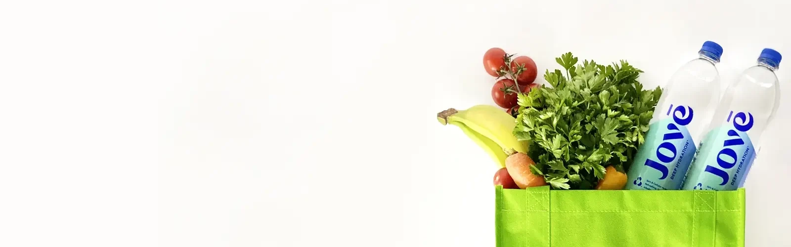 A green grocery bag with fruit, vegetables and bottles of Jove